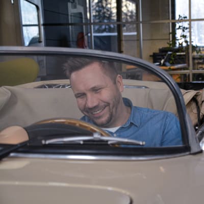 Roni Collin sitter i en gammala beige öppen Porsche. Han ler. Bilen är inomhus vid hans kontor.
