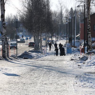 Stadscentra i vinterskrud. Personer går på trottoaren och bilar kör på vägen.