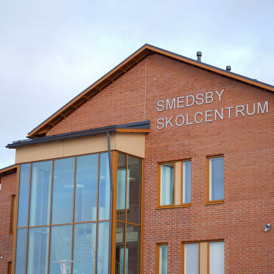 Närbild på en skolbyggnad i rött tegel. På väggen står det Smedsby skolcentrum.
