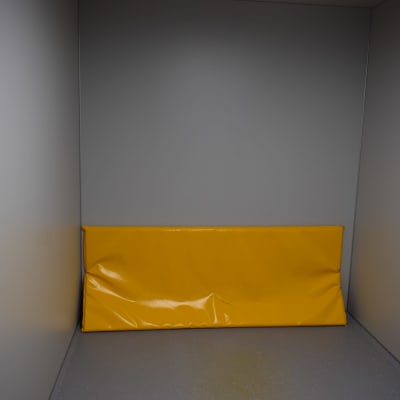 En gul madrass i ett grått rum. 