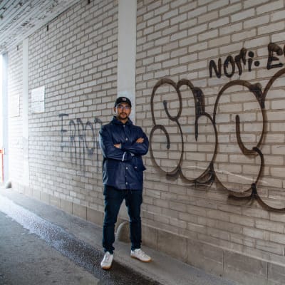 En man står invid en graffitimålning i en portgång.