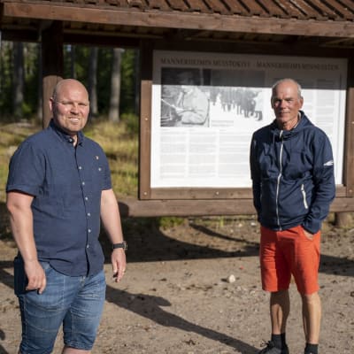 Tvä män vid en stor skylt som berättar om Mannerheim.