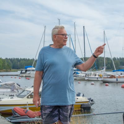 Christer Helenelund tittar bort och pekar åt sidan. Hammars småbåtshamn i bakgrunden.