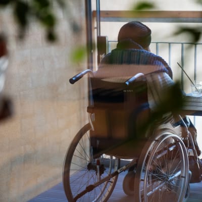 En person sitter i en rullstol och blickar ut genom fönstret.