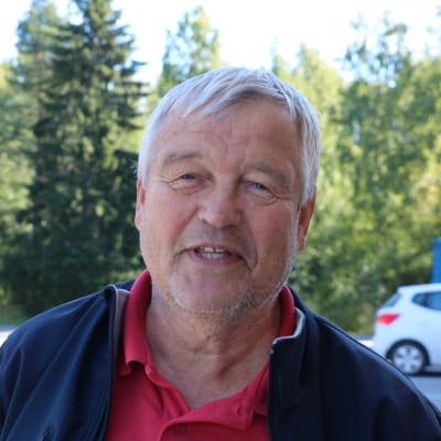 En man kort grått hår står på en parkering.