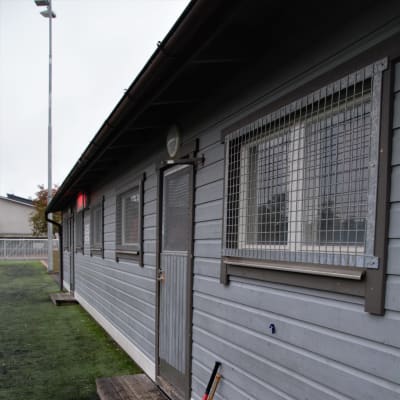 En grå avlång träbyggnad med omklädningsrum vid en idrottsplats.