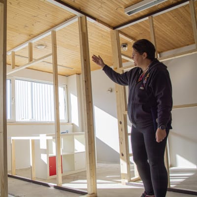 En kvinna visar runt i ett rum som håller på att byggas om till flera mindre rum.