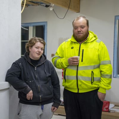 En kvinna och en man står vid en blivande vedeldad spis på ett husbygge.