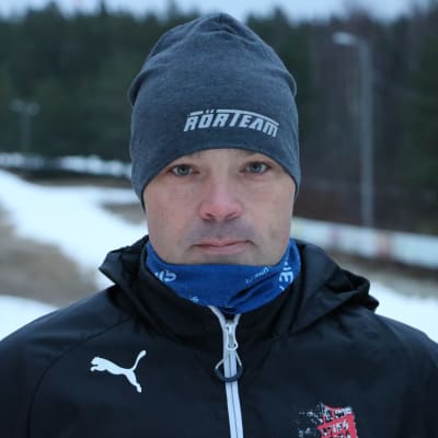 En man med mössa på huvudet står intill ett skidspår.