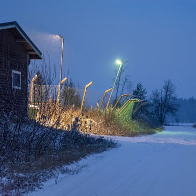 Träbyggnad och ett metallstängsel i ett mörkt vinterlandskap. 