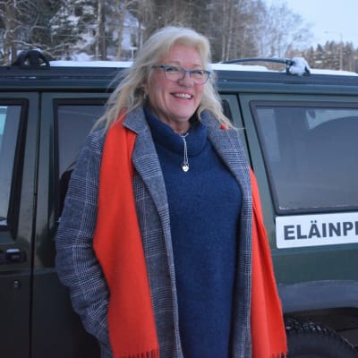 Kvinna med blont här står vid bil.