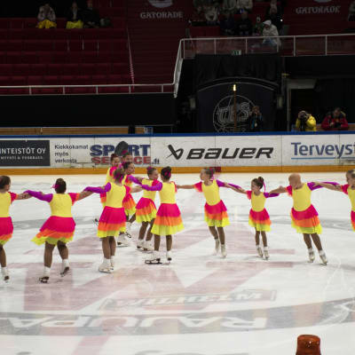 Flickor i färgranna klänningar skrinner i en formation som liknar tre ekrar i en cirkel.