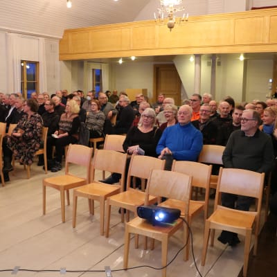 Människor som sitter på stolar i en sal.