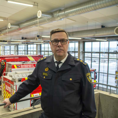 En person i räddningsverkets uniform står på en avsats i en brandstation. Bakom honom syns några räddningsfordon.