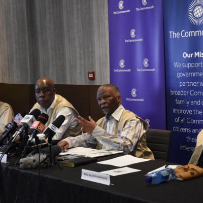 Fyra personer sitter bakom ett långt bord. Vid en plats finns det många mikrofoner. Där sitter Thabo Mbeki. Bakom honom syns Samväldets logotyp och texten The Commonwealth.
