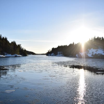 Vinterkväll i inre farleden i Barösund med solen som går ner över Bergvalla. Havet är öppet med enstaka simmande isflak.