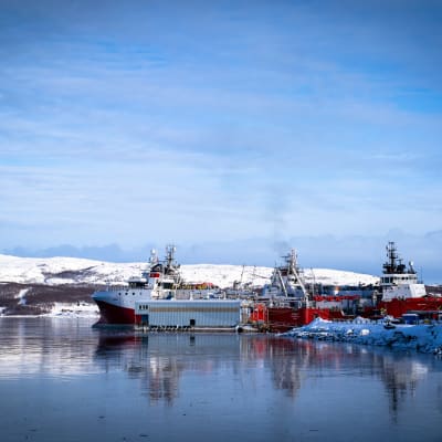 Rödvita ryska fartyg ligger vid en hamn. Snötäckta berg i bakgrunden.