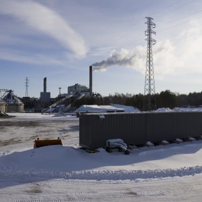 Finlands första geotermiska fjärrvärmeanläggning. Ett par gråa kontainrar, framför en industriell skorsten och en kraftledning. 