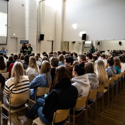 Elever sitter i en gymnastiksal och lyssnar på valdebatt