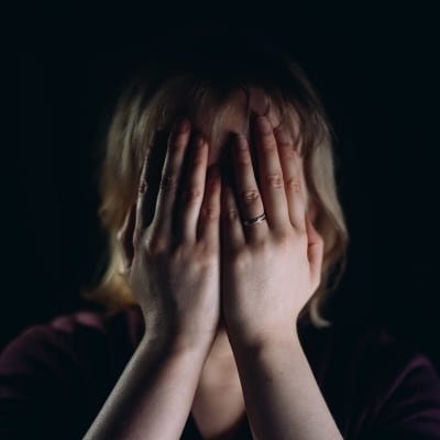 En person med vigselring på vänster hand håller händerna för sitt ansikte.