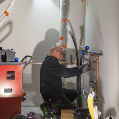 En rörmontör jobbar i ett blivande teknikrum i ett småhus som håller på att byggas.