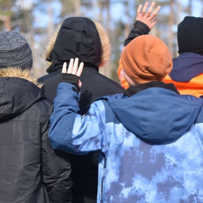 Fyra barn med ryggarna mot kameran viftar med händerna. De är vinterklädda.