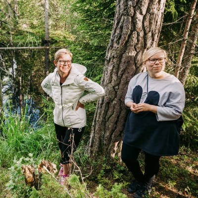 Krista Mikkonen och Saara Hyrkkö står vid en sjö i skogen.