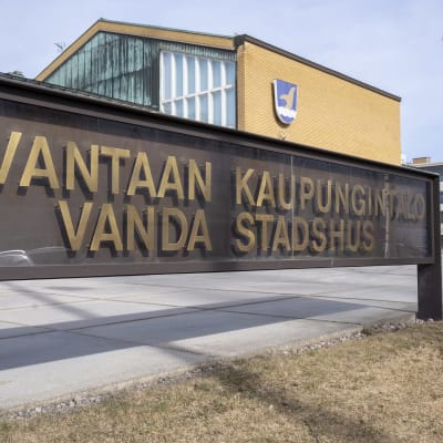 Enskylt med texten Vanda stadshus. i Bakgrunden syns stadshuset med kommunvapnet på väggen.
