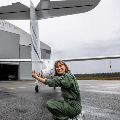 Kvinna i grön flygoverall inspekterar ultralätt flygplan