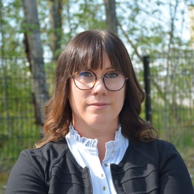 Kvinna i 35-40-årsåldern, mörkbrunt axellångt hår och glasögon, tittar in i kameran.