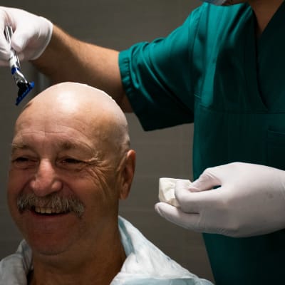 En man med sklligt huvud blir rakad av en sköterska. 