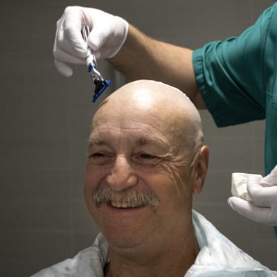En person rakar huvudet på en man som ler.