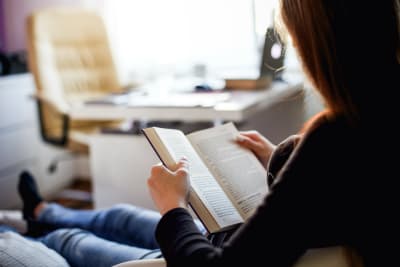 Kvinna läser bok på soffa.
