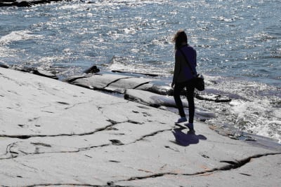 En siluett av en person som går längs klippkanten mot vattnet vid föboda i Jakobstad.