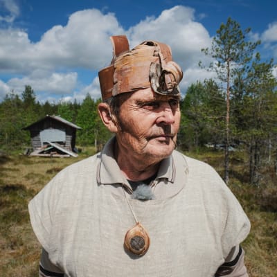 Erkki Kalliomäki päällään kyläpäällikön asu, tuohesta tehty päähine, puinen kaulakoru, pellavainen paita. Taustalla suomaisema, kuvattu Nummijärven Kammi-kylässä.