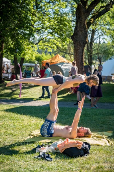 Mies ja nainen tekemässä akrobatiaa, nainen ilmassa miehen jalkojen päällä Natural High Healing Festivaalilla