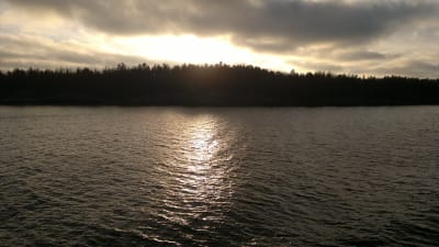 Solen går ner över en stor ö i skärgården och ljuset glittrar i vattnet.