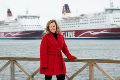 En kvinna i röd jacka står framför två av Viking Lines fartyg.