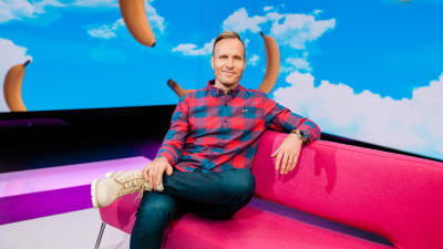Mikko Kekäläinen istuu vaaleanpunaisella sohvalla Puoli seitsemän studiossa.