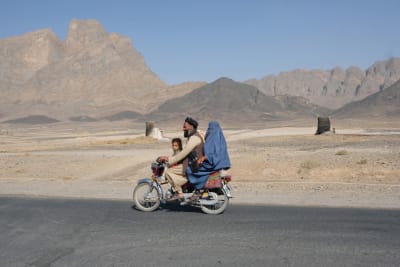 Mies kuljettaa moottoripyörän selässä siniseen burkaan pukeutunutta naista ja pientä lasta. 