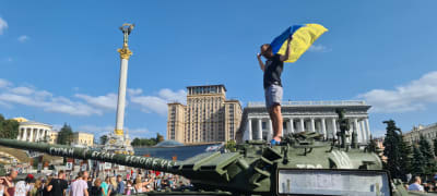 En man står på en förstörd rysk stridsvagn. Han håller upp den ukrainska flaggan.