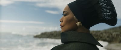 Närbild på en svartklädd, allvarlig och bestämd Ramonda (Angela Bassett) som står på en strand och ser ut över havet.