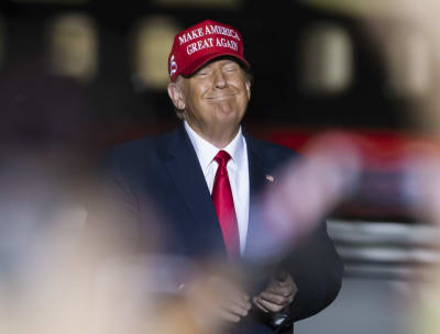 Donald Trump i kostym, röd slips och röd keps ler med ögonen stängda. På kepsen står det "Make America great again"