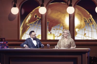Riku Rantala ja Jenni Poikelus istuvat Hengaillaan lavasteessa pöydän takana.
