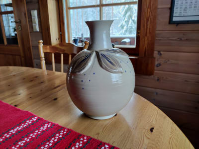 En vit-beige kruka med bladmönster står på ett bord.