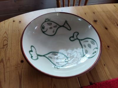 Ett vitt fat i keramik med tre glada fiskar med gröna konturer.