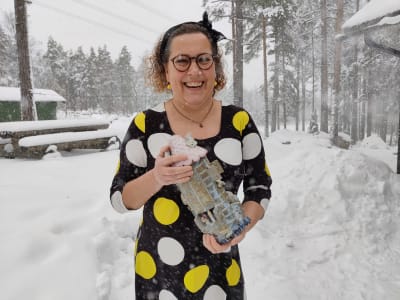 En kvinna står ute i snöyra med ett hus i keramik i händerna. Hon heter Nina Barrett.