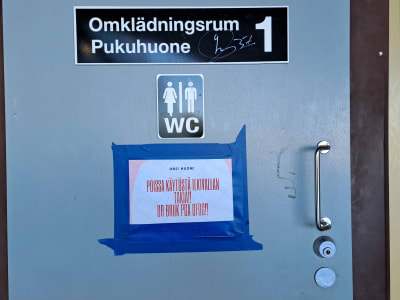 Ett papper på en dörr där det står på finska och svenska att ett omklädningsrum är ur bruk på grund av ofog.