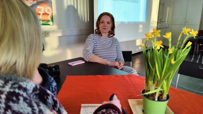 Katri Kulmuni framför valaffisch, med påskliljor på bordet.
