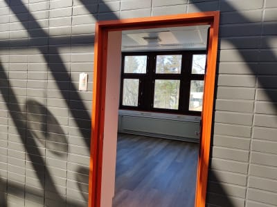 En orange dörrkarm och en grå vägg, inne i rummet ser man ett fönster.